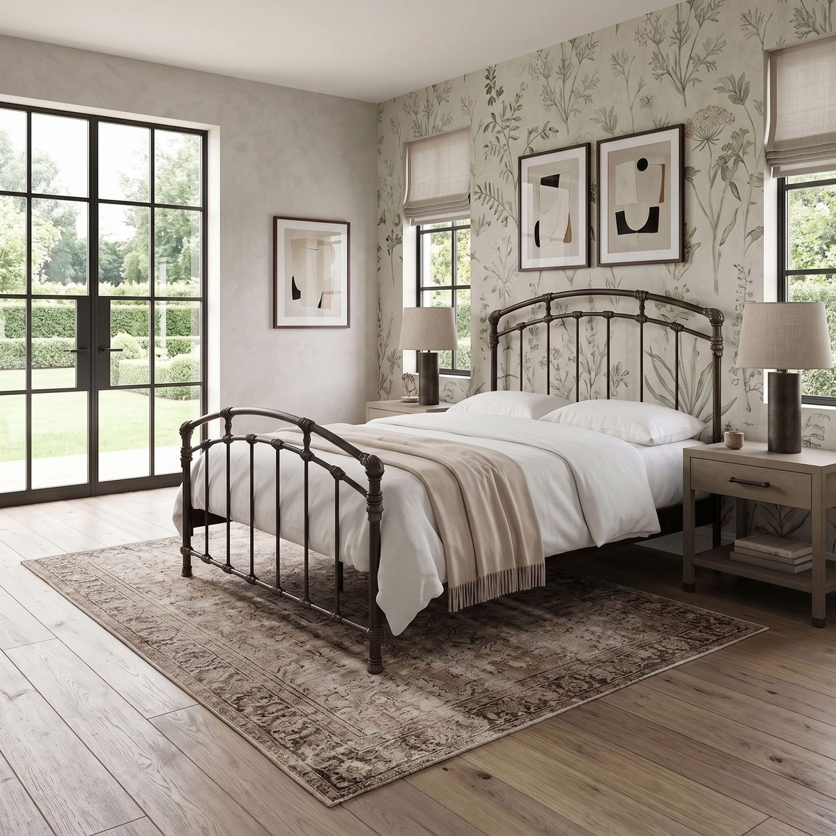Test Iron Bed by Wesley Allen in Aged Bronze finish in Queen size. A styled bedroom interior featuring a dark metal bed frame with a curved headboard and footboard, dressed in white bedding and a beige throw. The bed is placed on a distressed brown area rug over light wood flooring, flanked by matching bedside tables and lamps.
