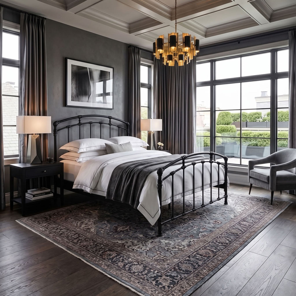 Test Iron Bed by Wesley Allen in Matte Black finish in Queen size platform frame with wood slats. A styled bedroom interior featuring a black metal bed frame with white bedding and a dark throw blanket, set on a large patterned area rug. The room has dark gray walls, tall windows with dark curtains, a modern chandelier, and a gray armchair.