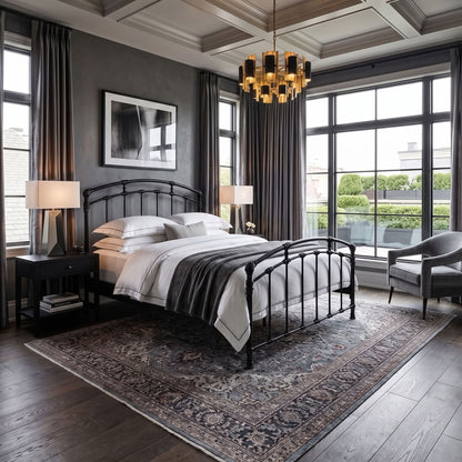 Test Iron Bed by Wesley Allen in Matte Black finish in Queen size platform frame with wood slats. A styled bedroom interior featuring a black metal bed frame with white bedding and a dark throw blanket, set on a large patterned area rug. The room has dark gray walls, tall windows with dark curtains, a modern chandelier, and a gray armchair.