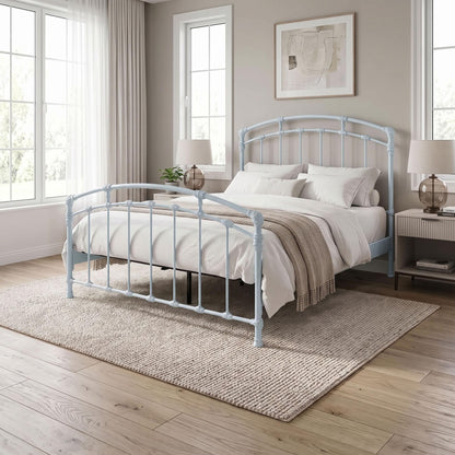 Test Iron Bed by Wesley Allen in Opaque Light Blue finish in Queen size platform frame with wood slats. A light blue metal bed frame with a curved headboard and footboard, styled in a bright, neutral bedroom with white bedding, a beige rug, and wooden floors.