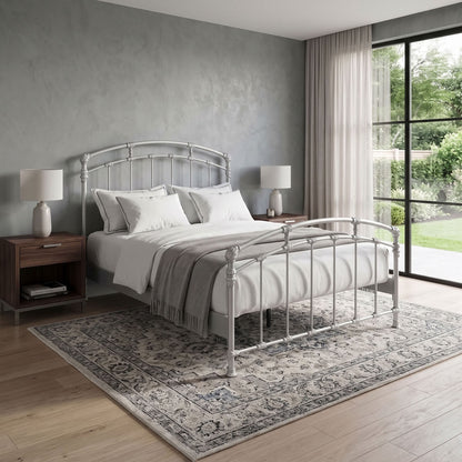 Test Iron Bed by Wesley Allen in Opaque Light Silver finish in Queen size platform frame with wood slats. A silver metal bed frame with a curved headboard and footboard, styled with white bedding and a gray throw blanket, set on a patterned area rug in a modern bedroom.