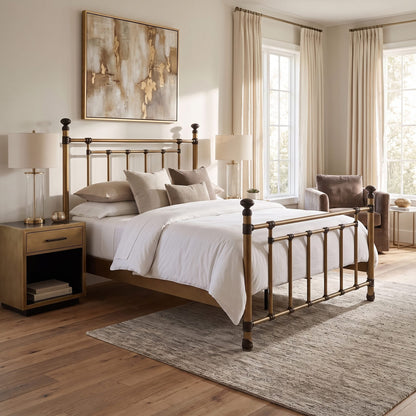 Blake iron bed 1094 in Aged Brass finish, queen size, by Wesley Allen for Matriae, styled in a warm bedroom with gold-framed art and a matching nightstand.