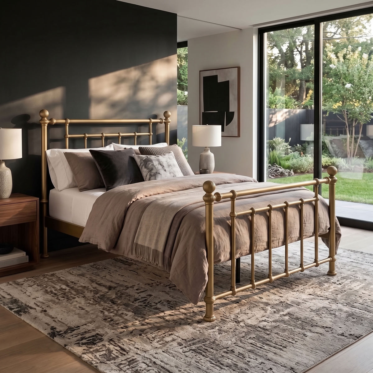 Revered Iron Bed by Matriae in the Opaque Gold finish queen size with a wood slats platform bed frame. A brass metal bed frame with turned posts and curved headboard and footboard, styled in a modern bedroom with beige and brown bedding, a patterned rug, and a large window overlooking a garden.